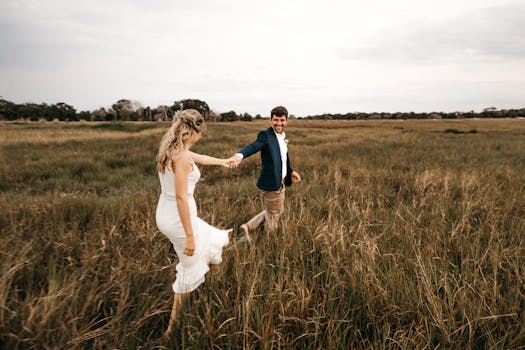 Happy couple holding hands and walking through a grassy field, embracing love and freedom.