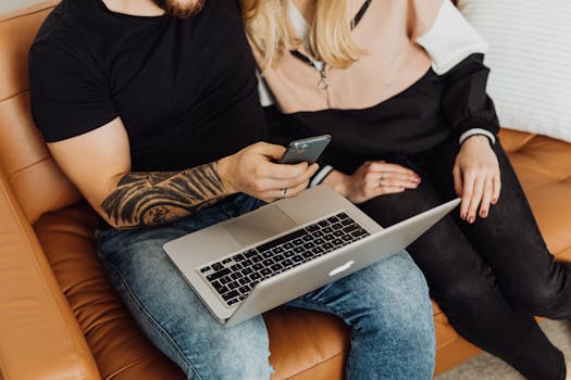 A young couple sitting on a sofa using a laptop and a smartphone together.