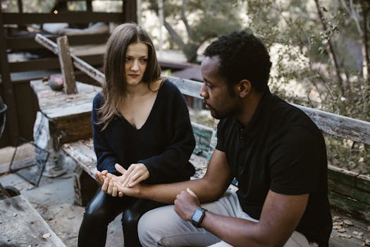 A couple in an emotional conversation on a rustic outdoor bench, conveying tension and concern.