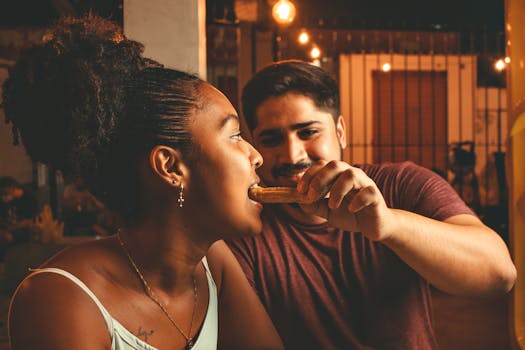 A couple enjoying a night out, sharing a churro under warm lights, expressing love and joy.